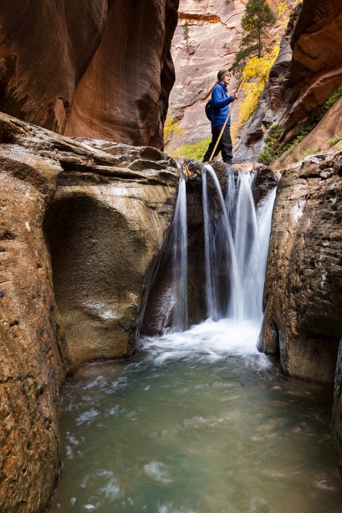 A man standing above a waterfall in orderville slot canyon with a walking stick.