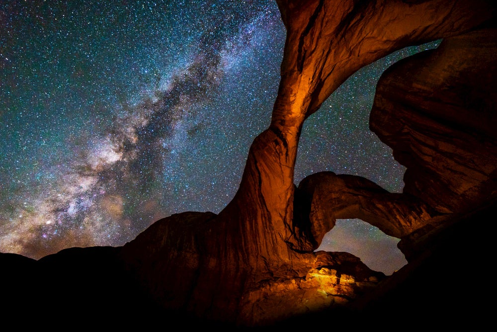 Twisting red rock arches in Moab, utah with the milky way seen in the sky in the background 