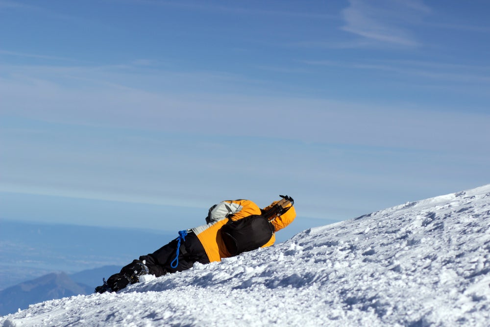 View from behind of hiker falling over in the snow on mountainside.