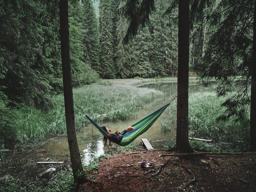 Woman sleeping in green hammock by a river in the forest.