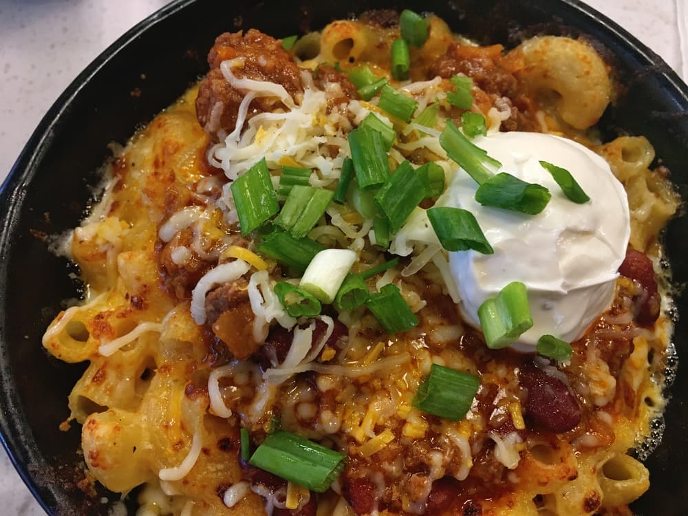 chili mac and cheese topped with cheese, sour cream, and chives