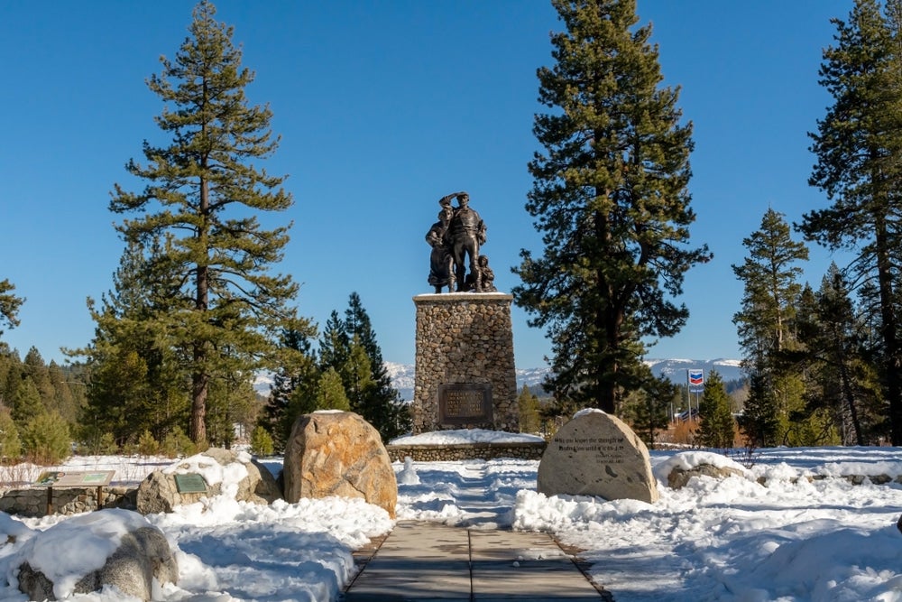 snow covers the ground in front of a metal statue at the Donner Memorial State Park and Emigrant Trail Museum