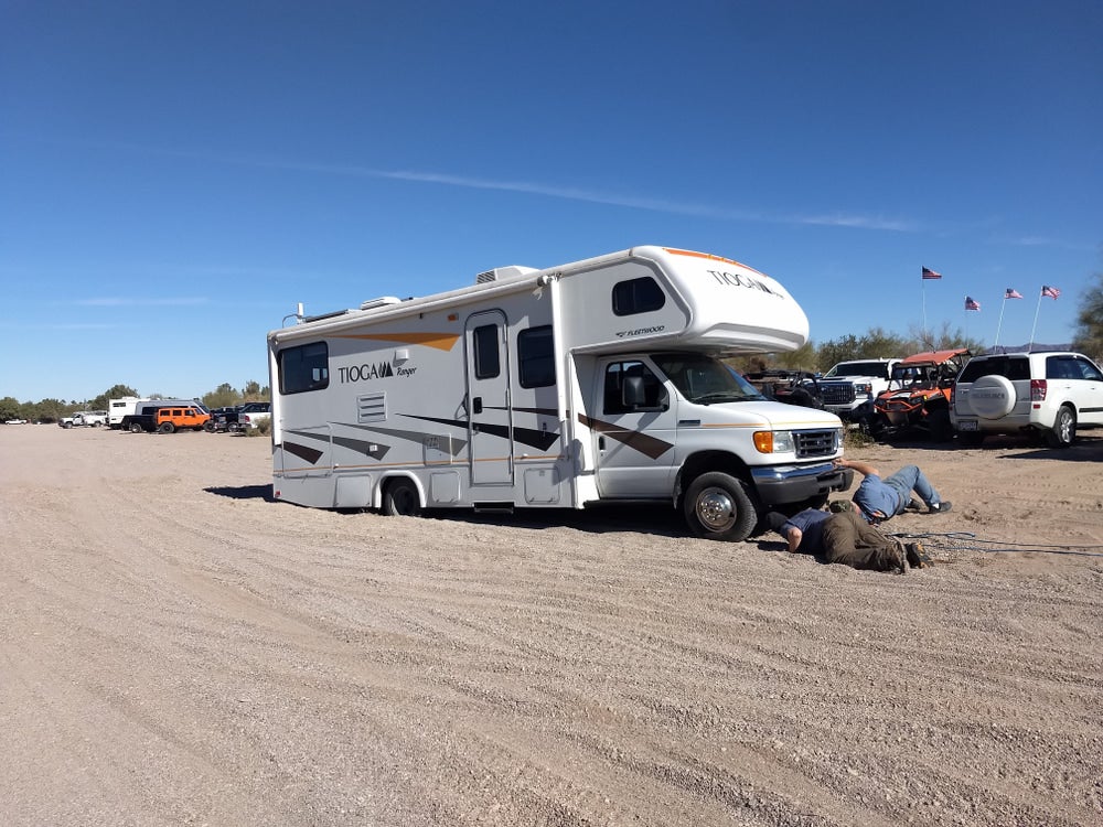 Men sprawled on ground in front of RV that is stuck in the sand.