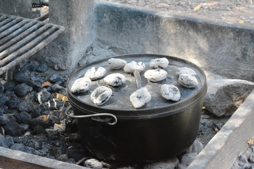 campfire cooking with dutch oven sitting on coals with coals on top of lid