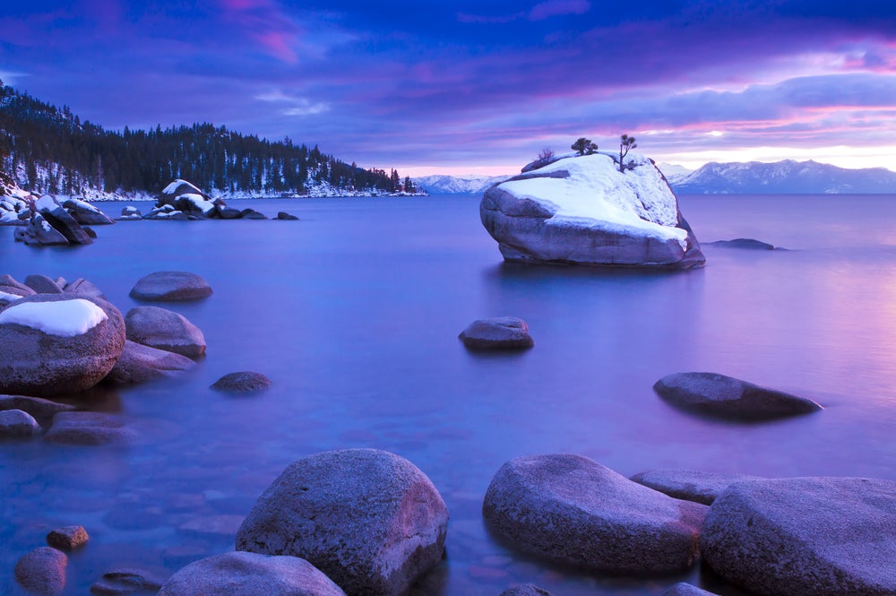 Pink sunlight of dusk shining on the snow capped rocks sticking out of Lake Tahoe.