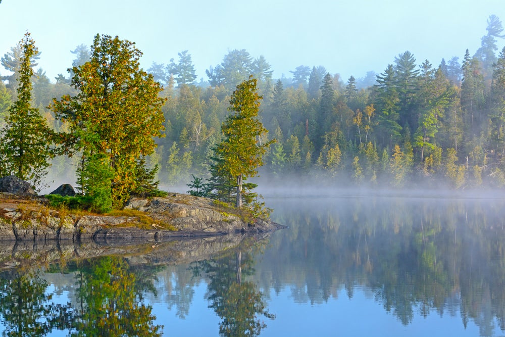 a wide angle view of fog over lake in minnesota with trees and stone on island 