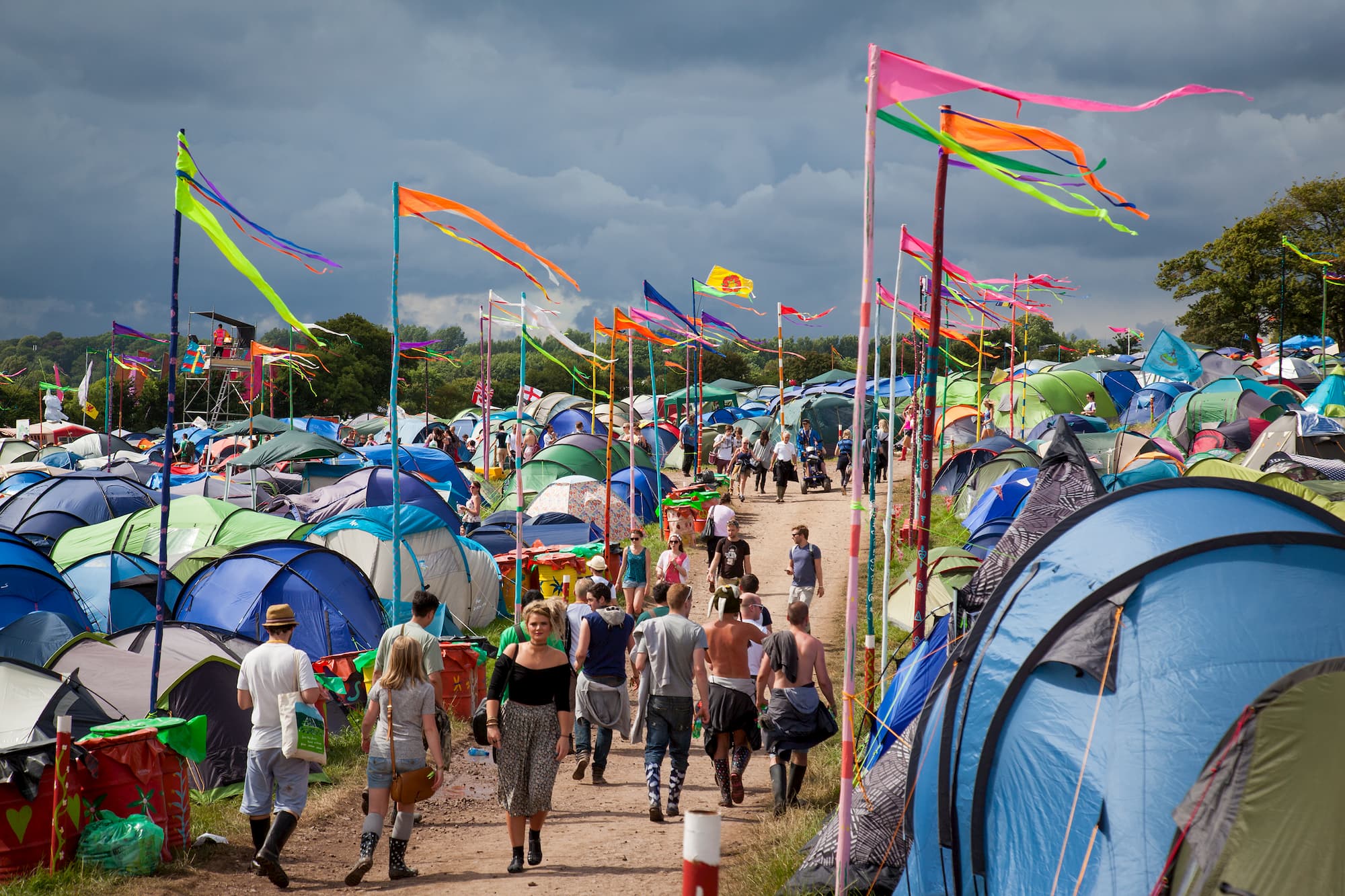 Groups of blue tents at a music festival with people walking along a path to the right