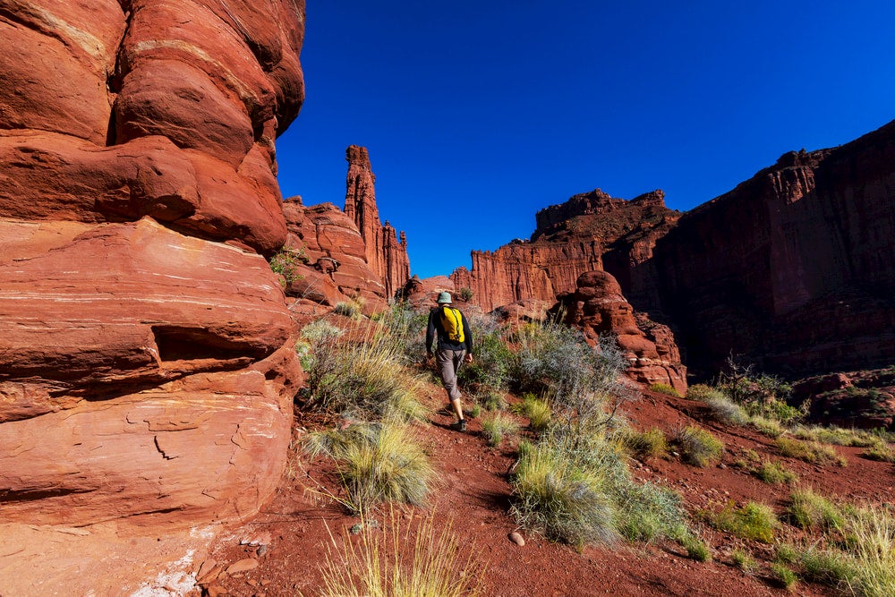 Man hiking among red rocks in moab, utah with Fisher Tower in the background 