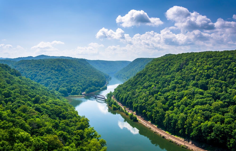 Landscape view of the New River Gorge with reflective river and green trees beside river