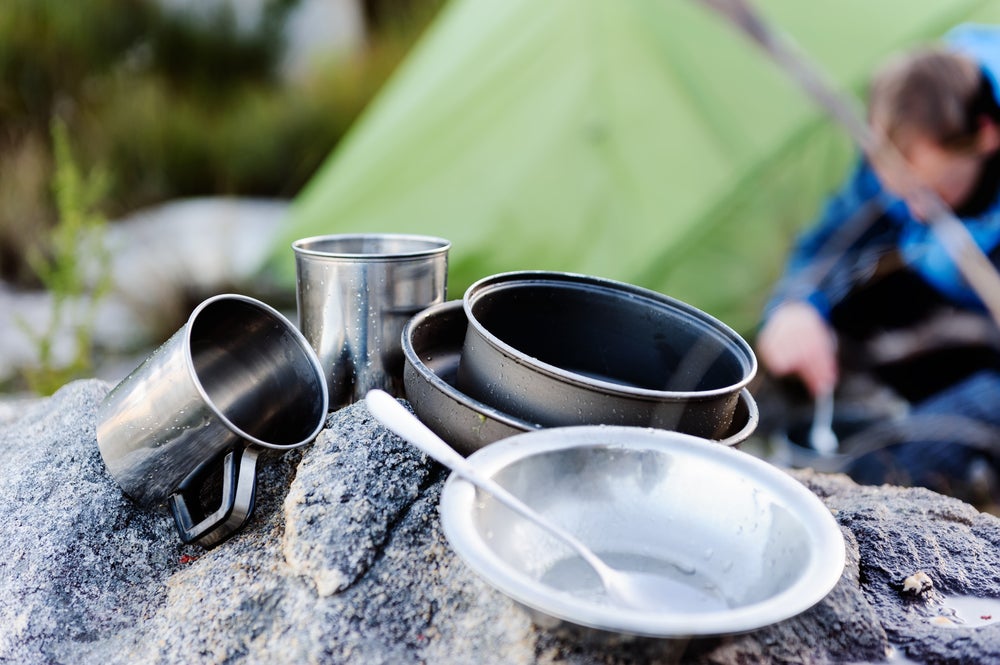 Camping mess kit and utensils resting on a rock after cleaning