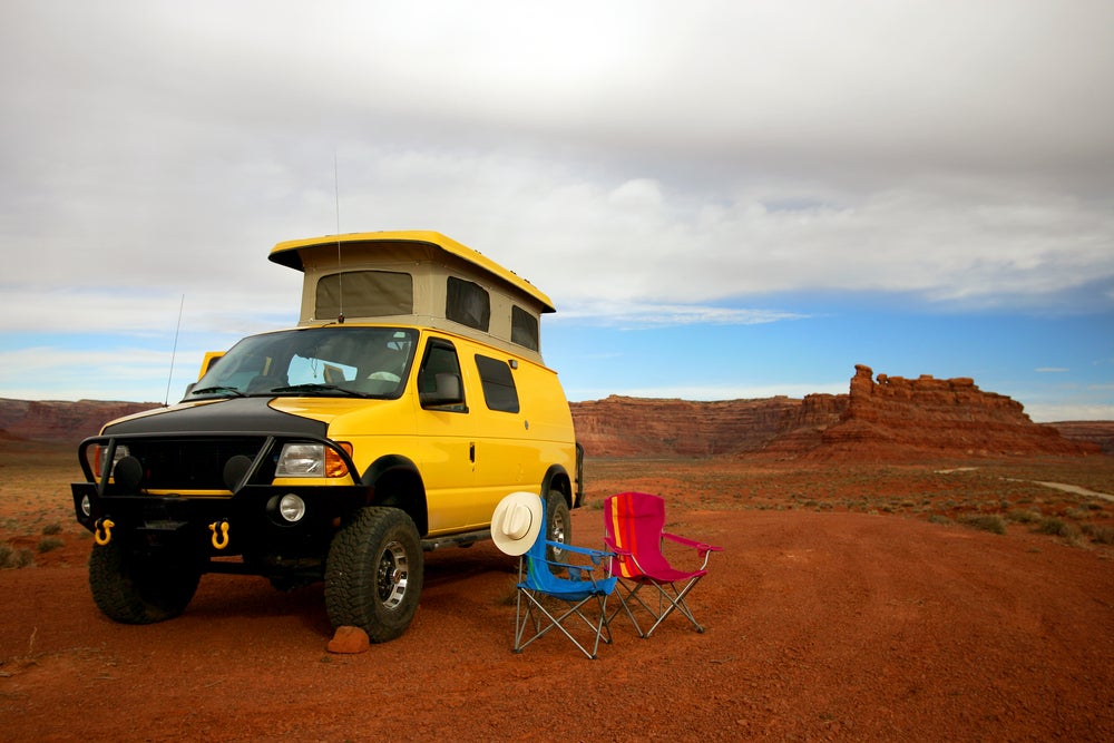Yellow adventure van with a pop up top parked beside camp chairs in Utah desert.