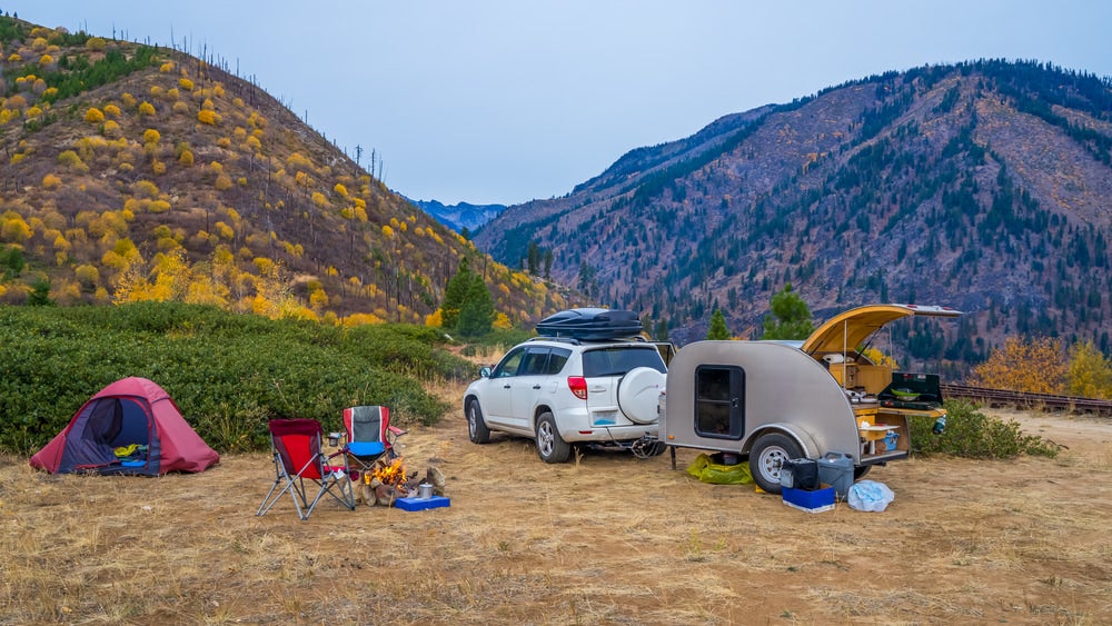 camping trailer attached to an suv parked in a desert campsite in front of tall hills