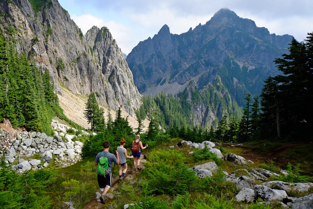 Three people backpacking on a trail with mountains in the background 