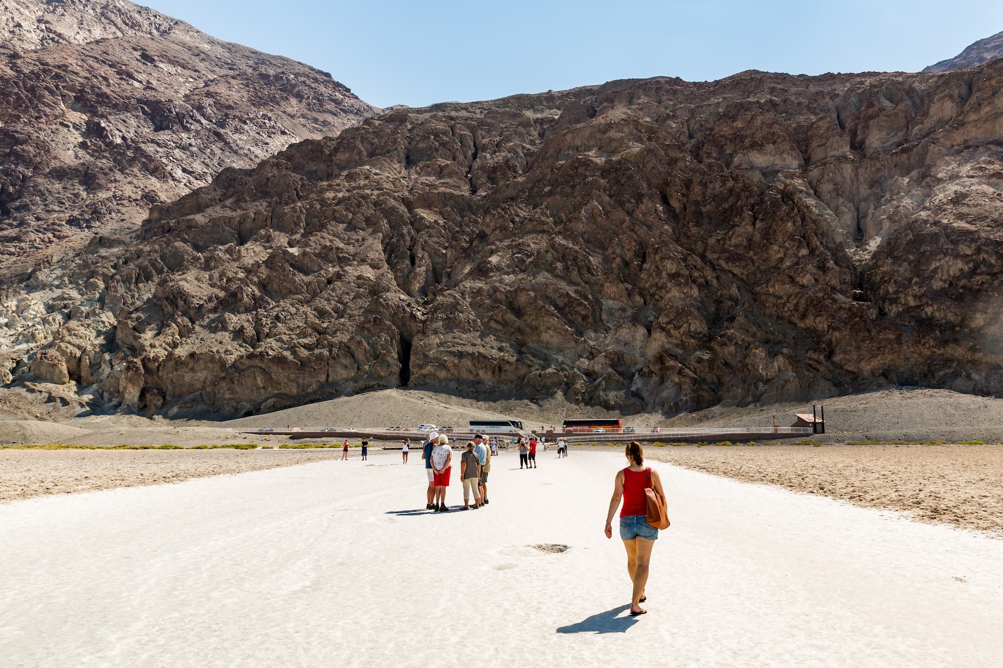 a woman walks toward a crowd and a mountain on a desert plain in death valley national park
