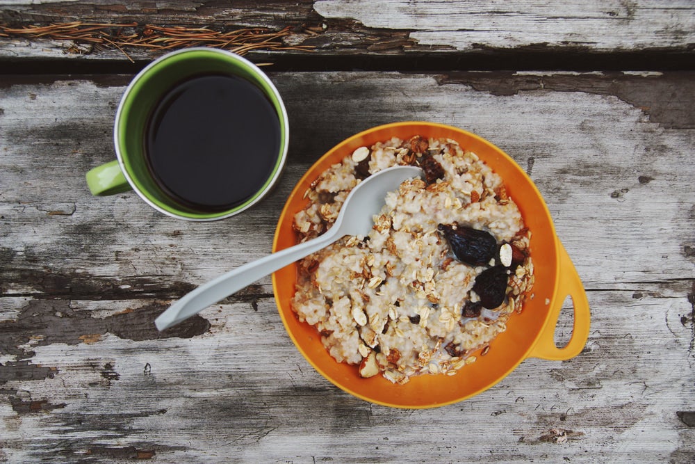 Bowl of oatmeal beside a mug of coffee on an aged wooden table