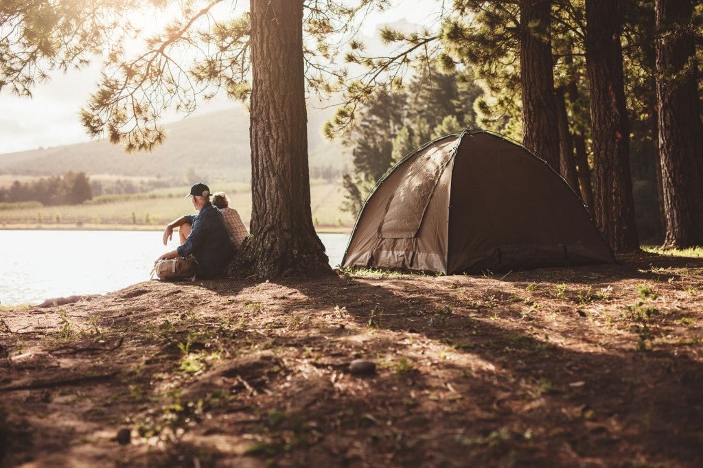Couple sitting by the edge of a lake in the sun beside their tent