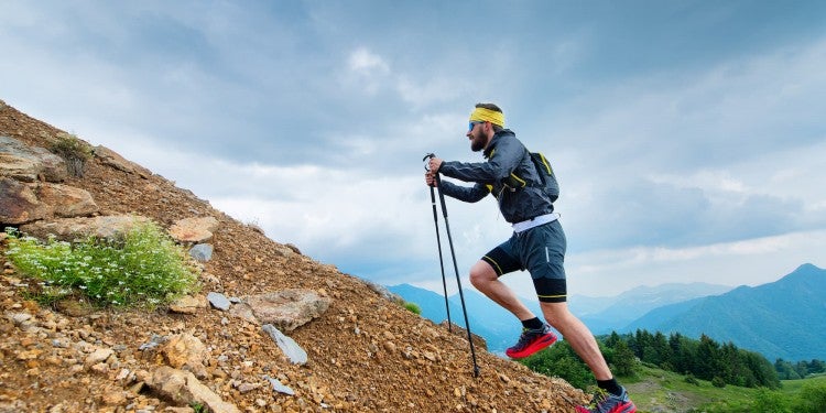 man hiking uphill with trekking poles.