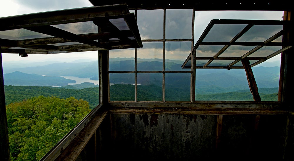 Large windows inside a fire tower tilted open to display green rolling hills and a river 