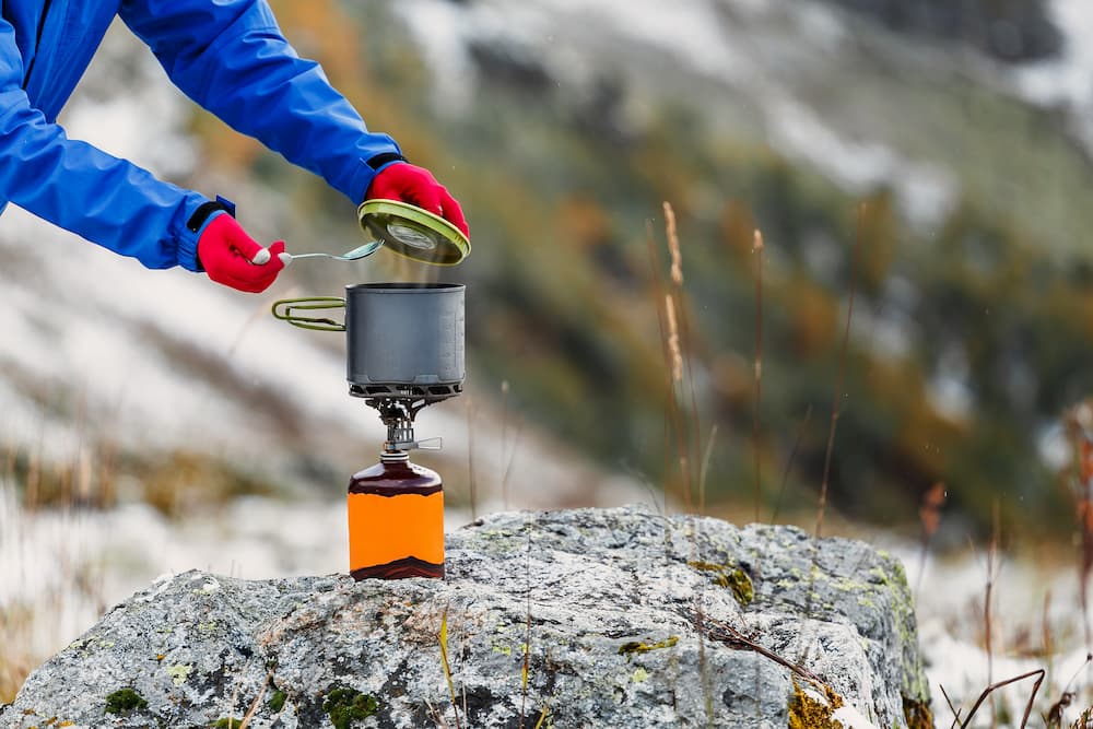 a camper checking on a meal cooking on a backpacking stove