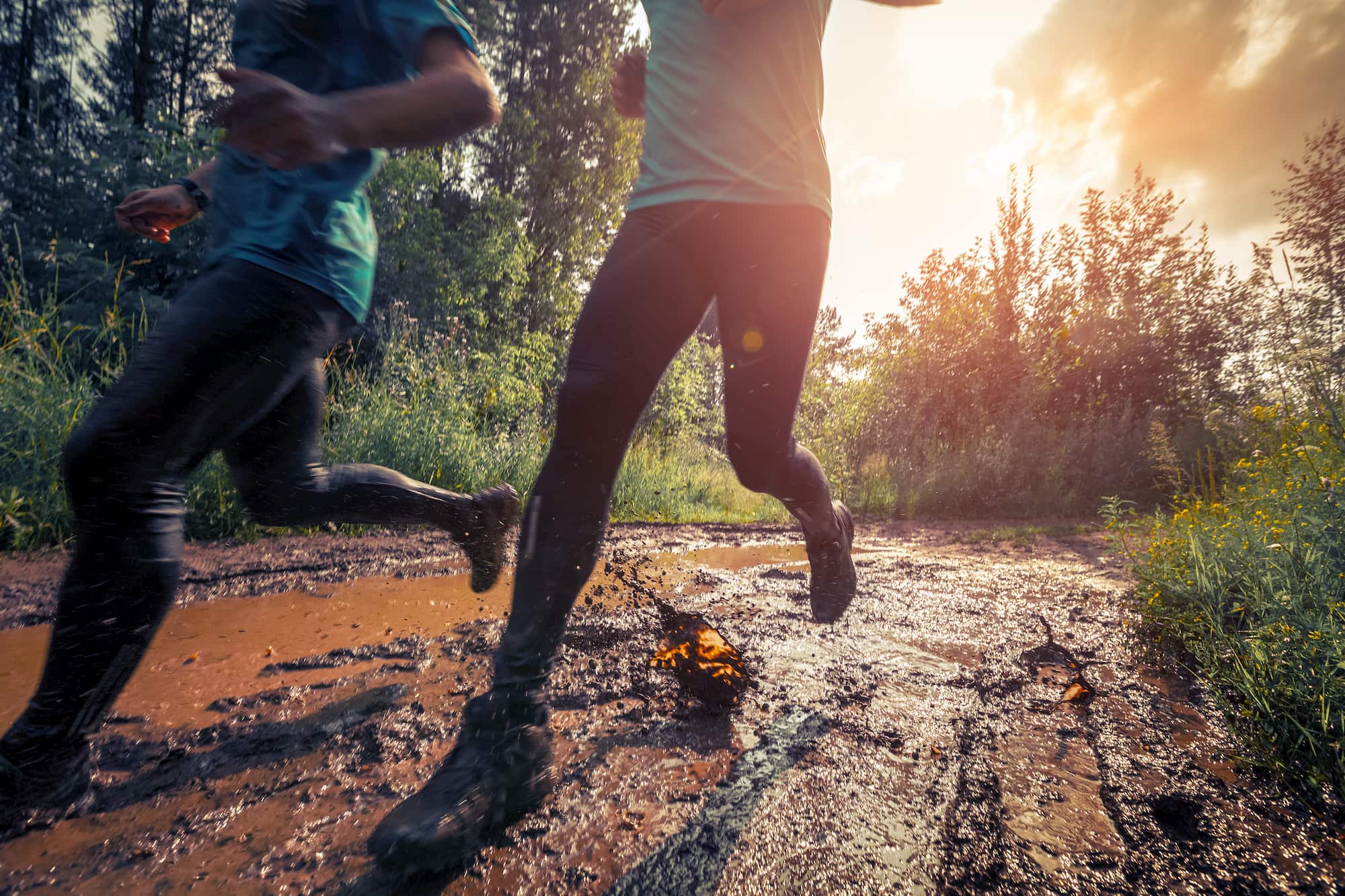 two runners on a muddy trail at sunset with the camera focused at their hiking and running shoes