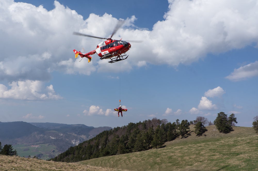 Injured person on a stretcher gets airlifted by a helicopter out of the back country.