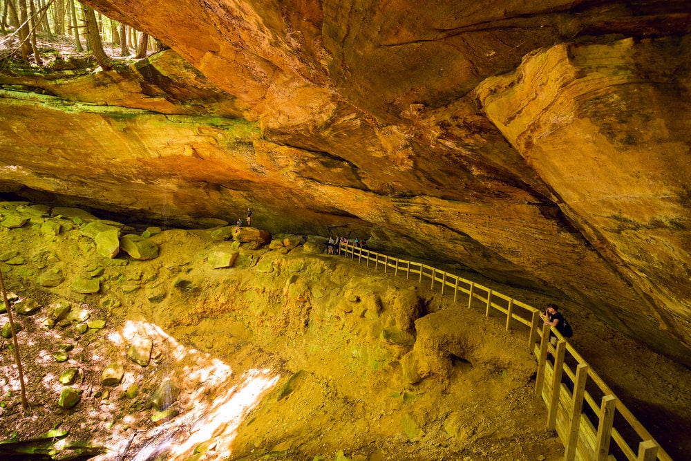 People walk behind a wooden railing leading around a walkway within a wide cave.