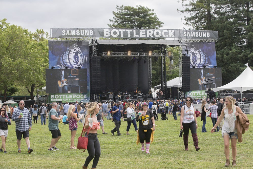 Concert stage and large group of people walking on grassy field