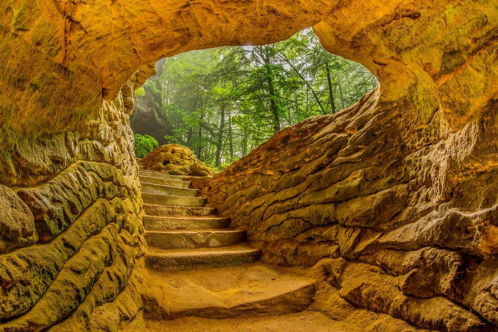 Yellow colored rock wall formation with natural staircase winding through an underground walkway.