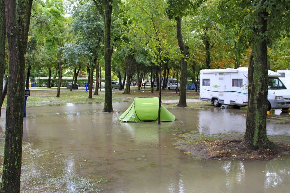 Green tent set up in the middle of a flooded campsite beside an RV