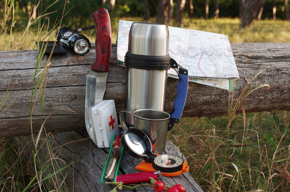 A knife, first aid kit, headlamp, compass placed on a log.