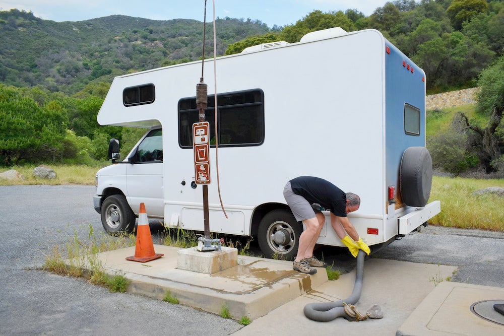 Man wearing rubber gloves and draining his r.v. toilet with a hose.