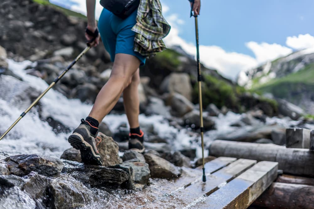 ground level view of hiker with trekking poles crossing a rocky river