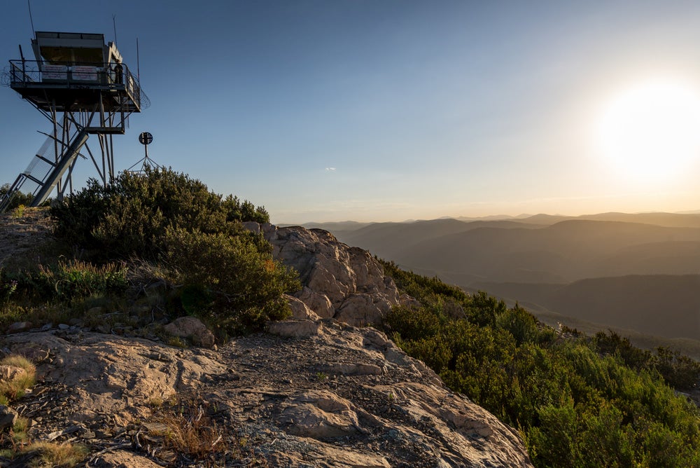 View of fire tower on rocky hillside with rolling mountains in background