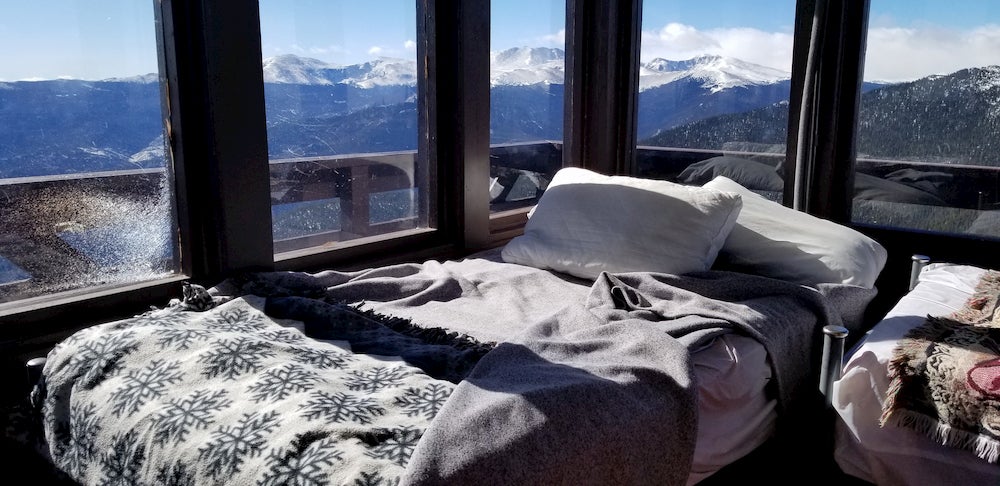 View of bed inside of a fire tower displaying with mountain views visible outside