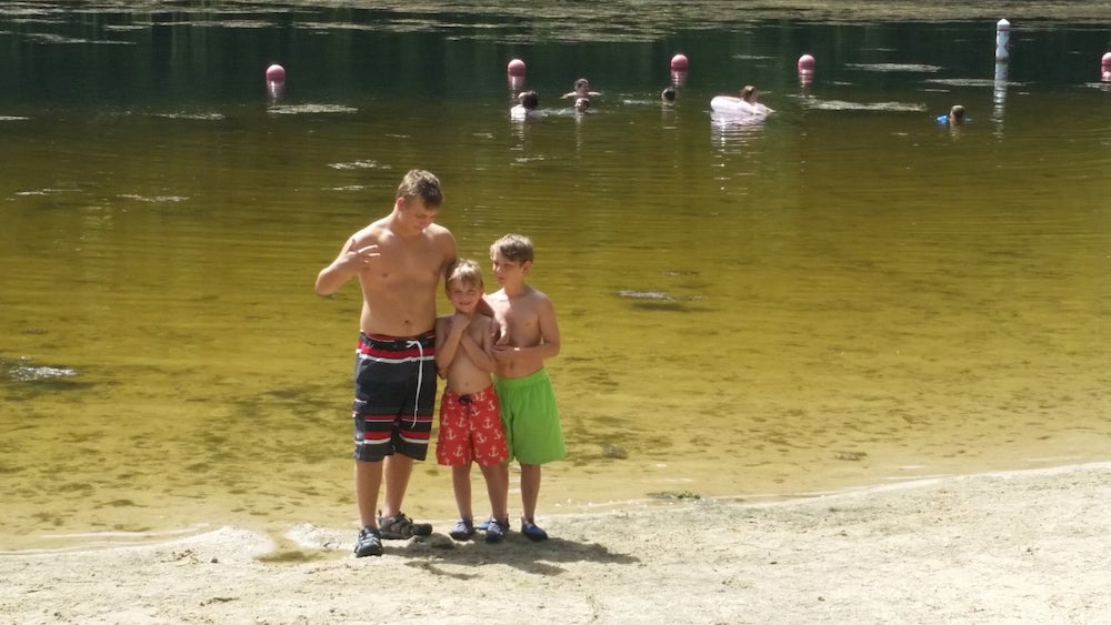 Three boys standing in front of a lake 