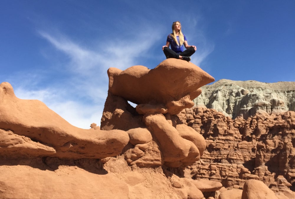 Woman sitting cross legged on rock formation in Goblin Valley