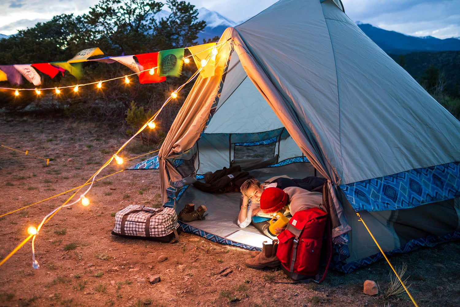 two people lying in a sleeping bag in a tent strung with string lights