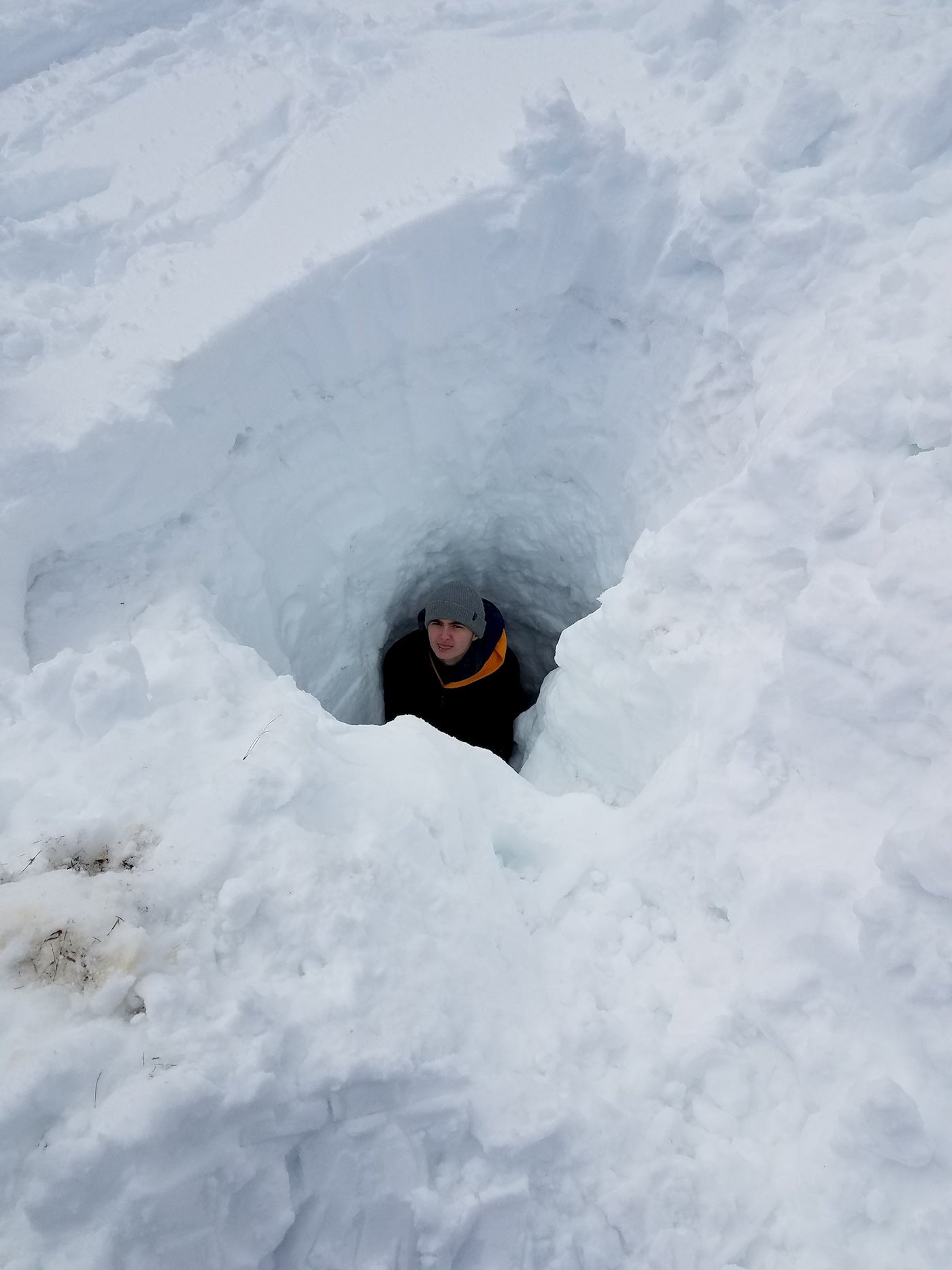 Teen sitting in deep dug hole learning about snow safety.