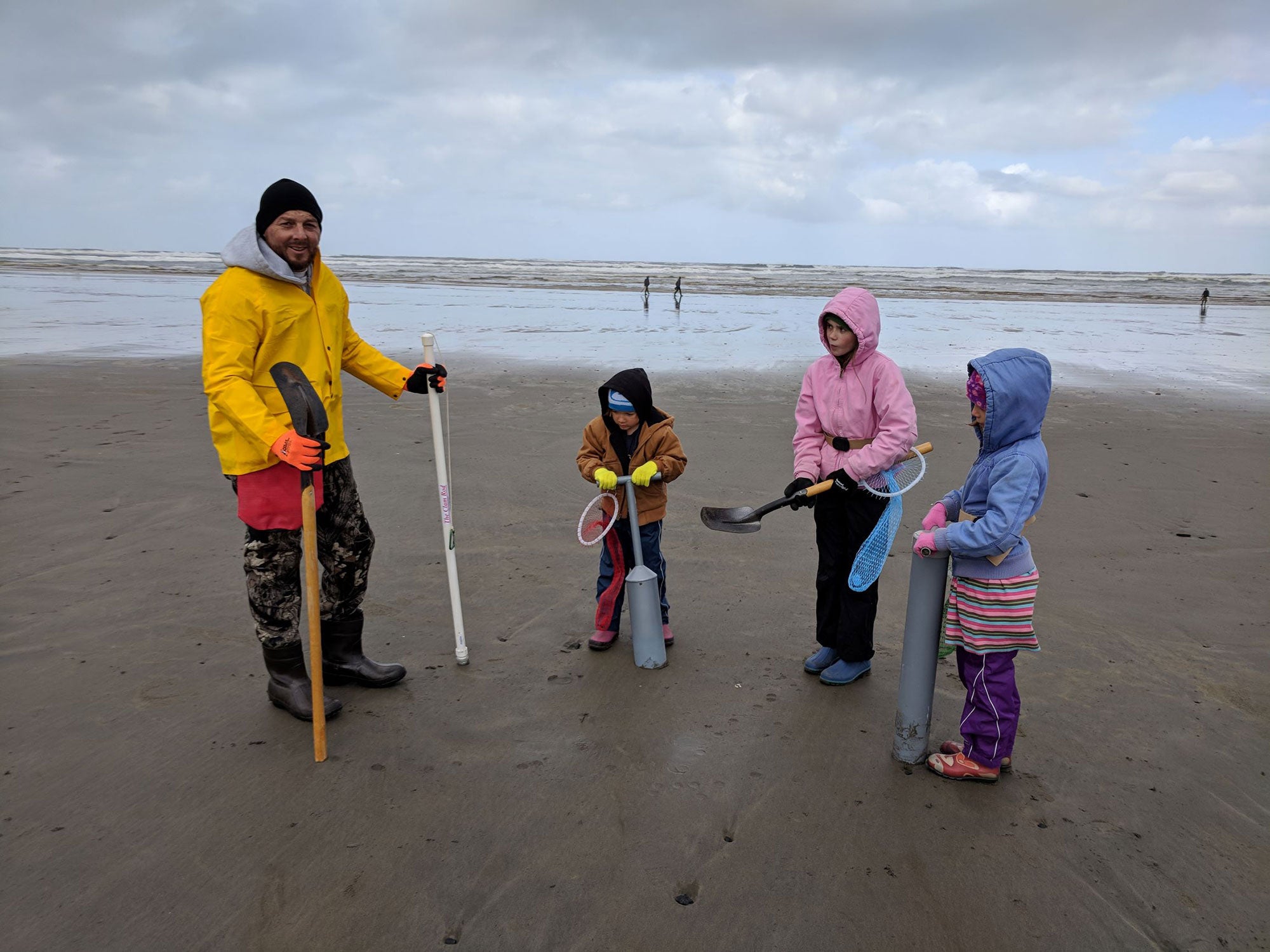 a family holding shovels wearing rain gear go digging for clams