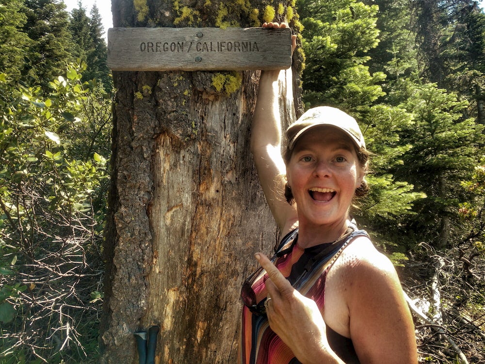 heather anderson posing in front of a wooden sign at the oregon california border