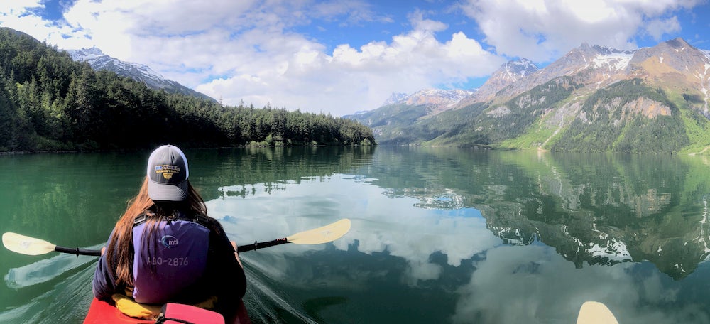 Woman kayaking in lake with large mountain on and trees in far distance