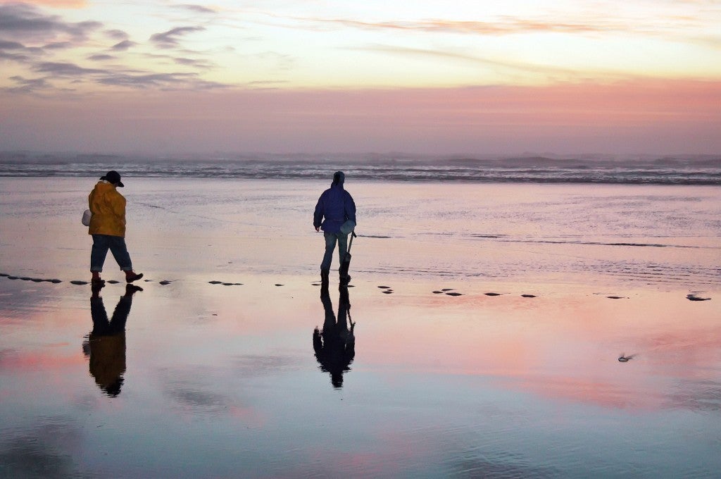 two people wearing rain gear hunting for clams on the beach at dusk