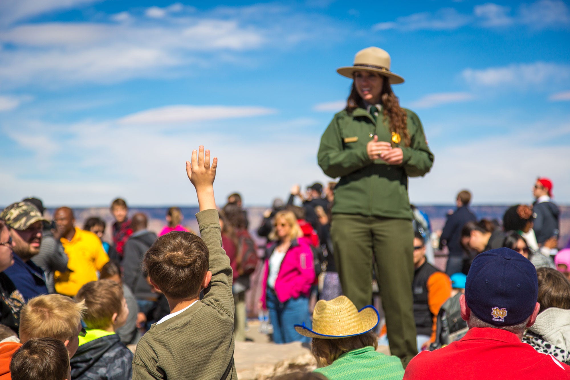 Young boy raises his hand to ask a Park Ranger a question. 