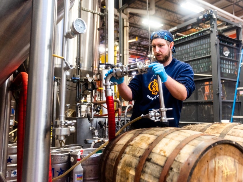 Man brewing beer with barrels in front of him 