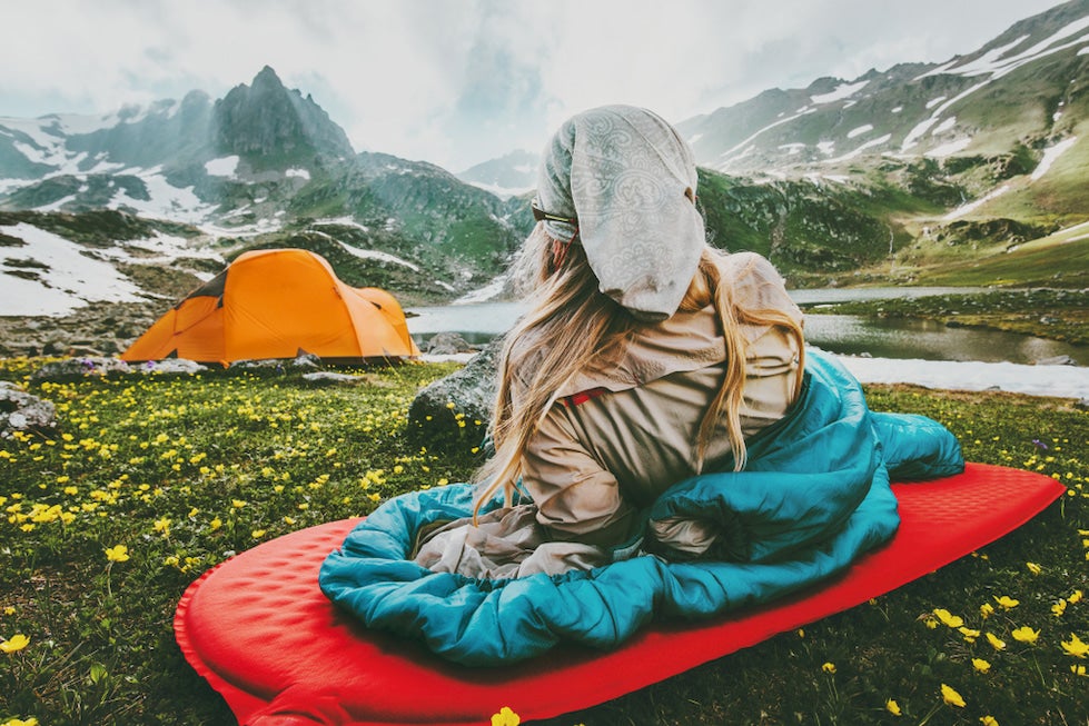 Woman lounged in sleeping bag surrounded by alpine landscape.
