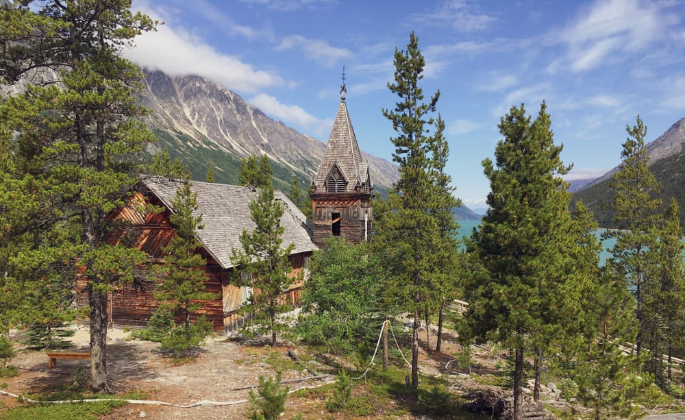 Old gothic style cabin with mountains and trees in background 
