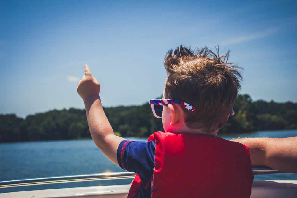 Boy on boat pointing at lake 