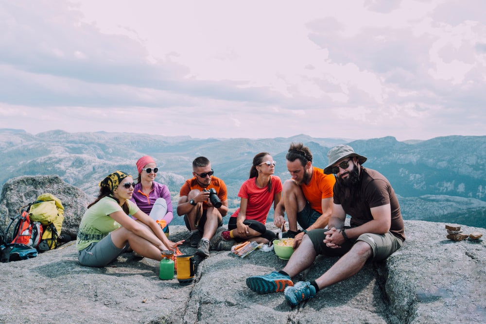 6 hiker friends eating lunch on a mountain surrounded by gear