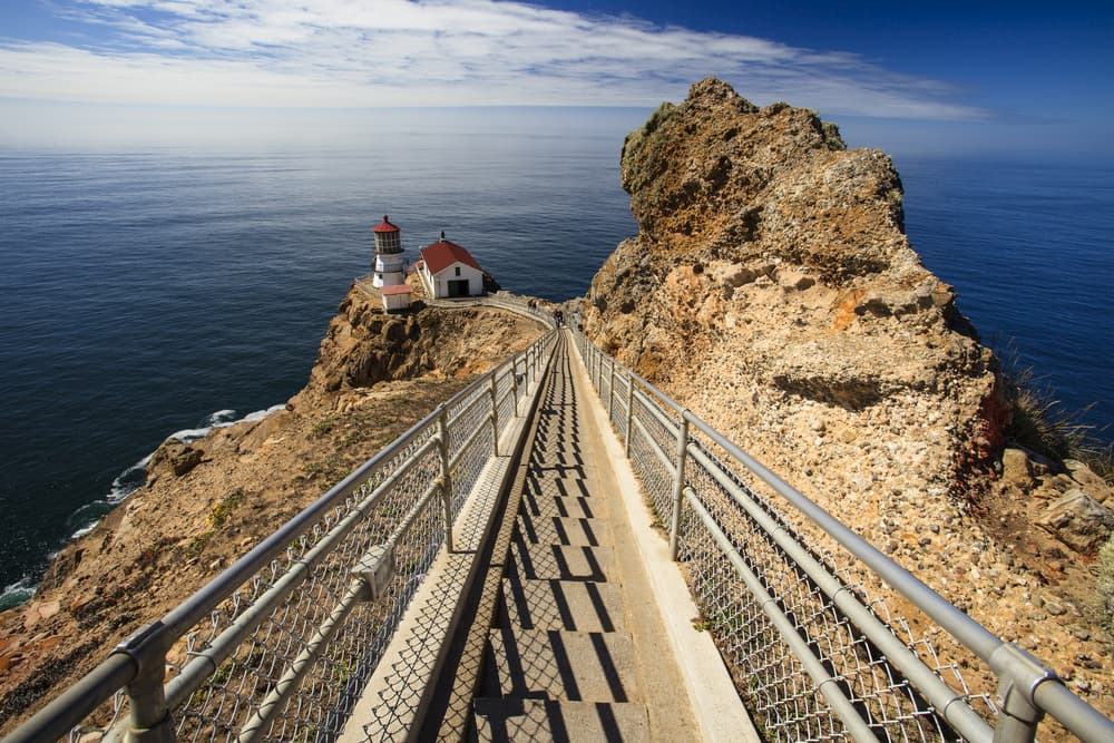looking down staircase toward Point Reyes lighthouse perched on rocky outcropping in the pacific ocean