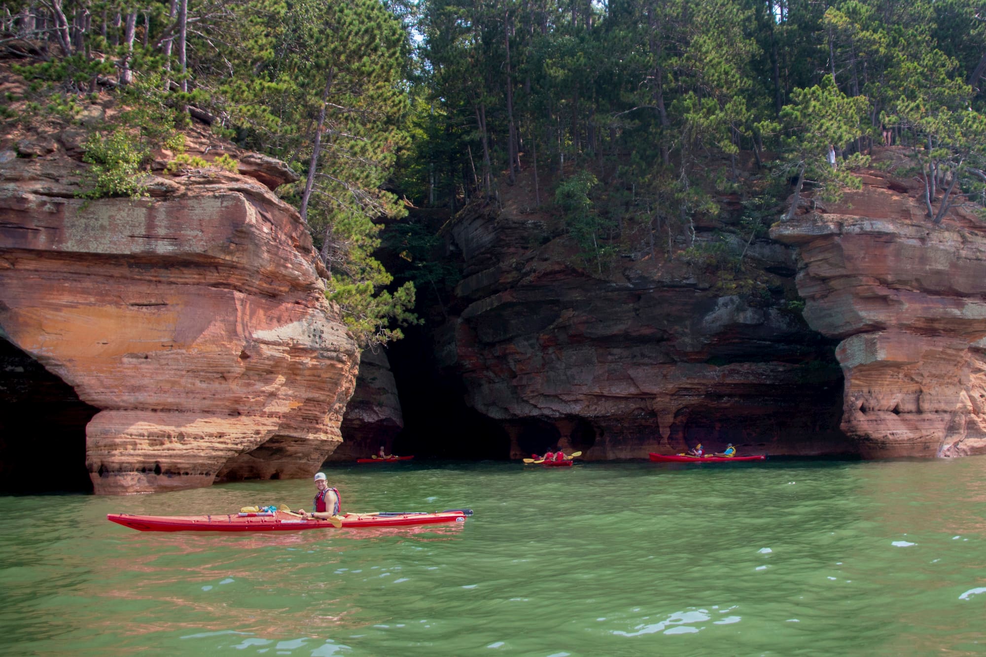 long distance shot of kayaker in red kayak on green water with red rocks behind them